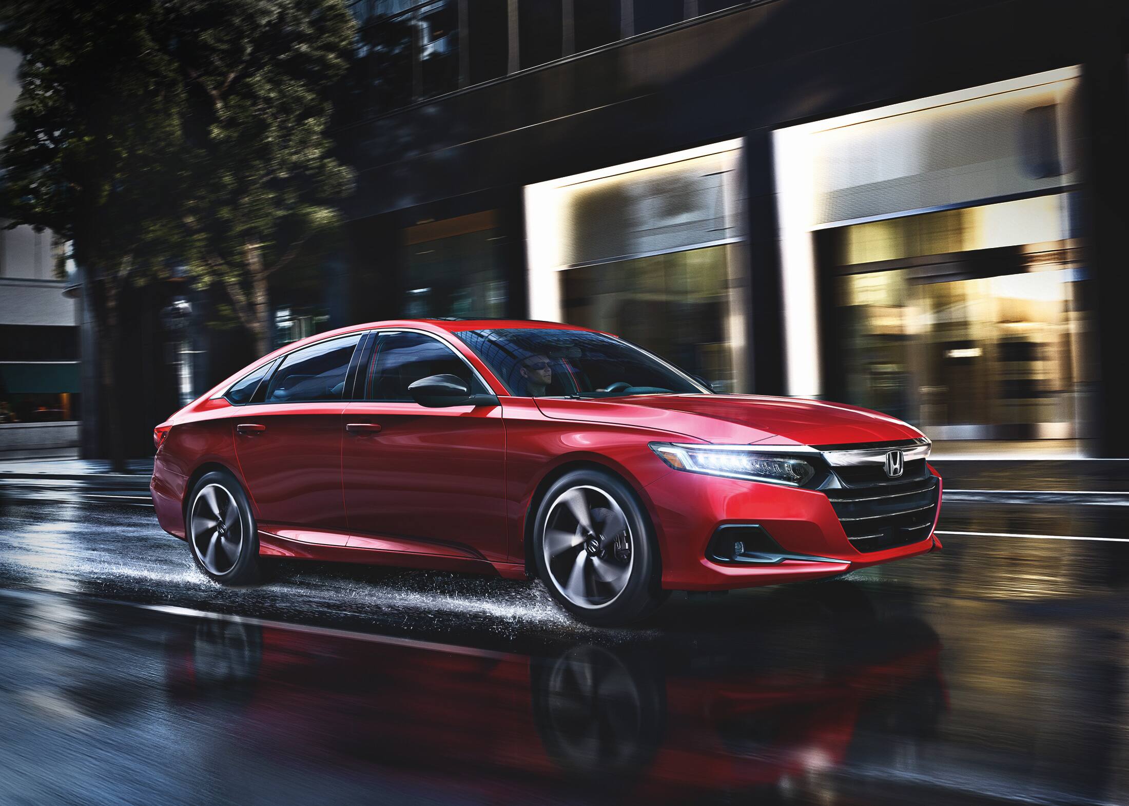 Front passenger-side view of the 2022 Honda Accord Sport 2.0T in San Marino Red driving through an urban environment.