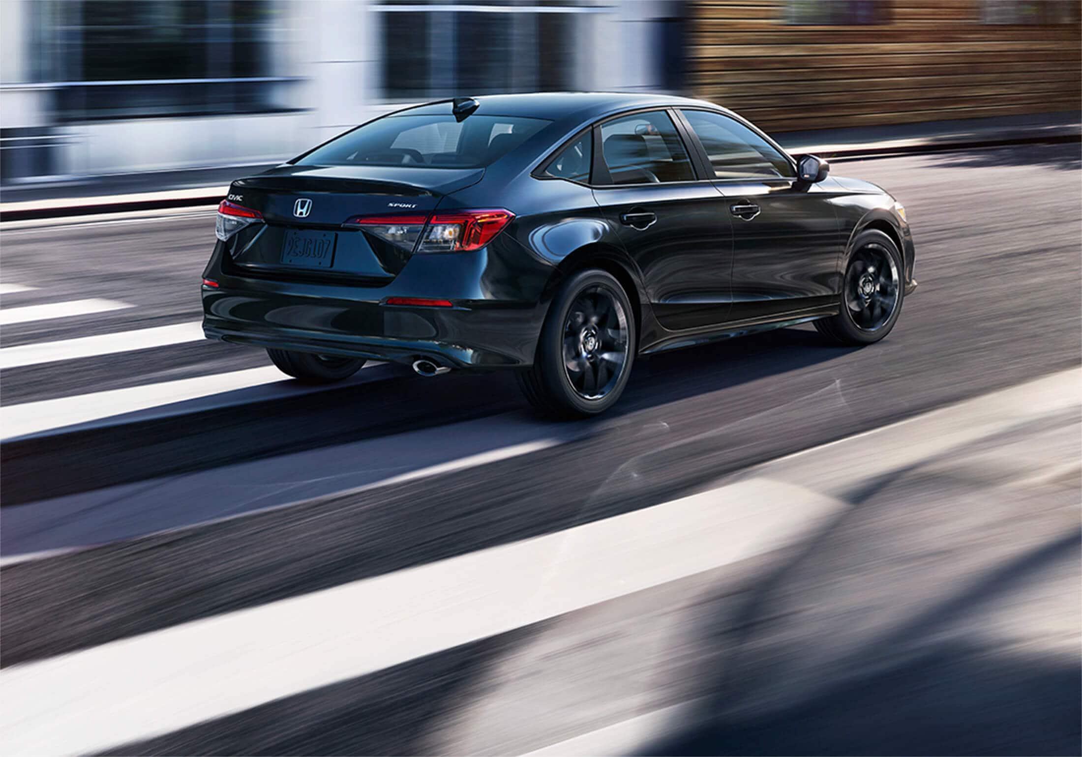 Rear passenger-side view of the 2023 Honda Civic Sport Sedan in Crystal Black Pearl, making a right turn on a city street. 